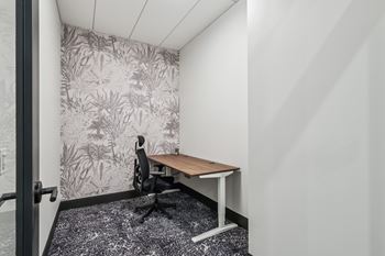 A small room with a desk and a plant pattern wallpaper.
